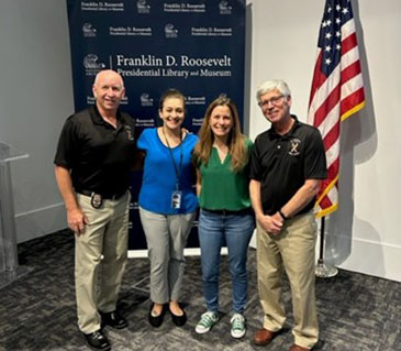 Retired Lieutenant Jimmy Donohoe (Pensacola Police Department), Mara Santiago (Administrative Assistant, Dutchess County All Abilities Programs), Dana Hopkins (Dutchess County, All Abilities Program Director) and Retired Captain Bill Cannata (Westwood, Massachusetts Fire Department) stand in front of the FDR Presidential Library and Museum “Step and Repeat” and an American flag, after the day’s training, which received evaluation scores of over 95% 5 out of 5 ratings.