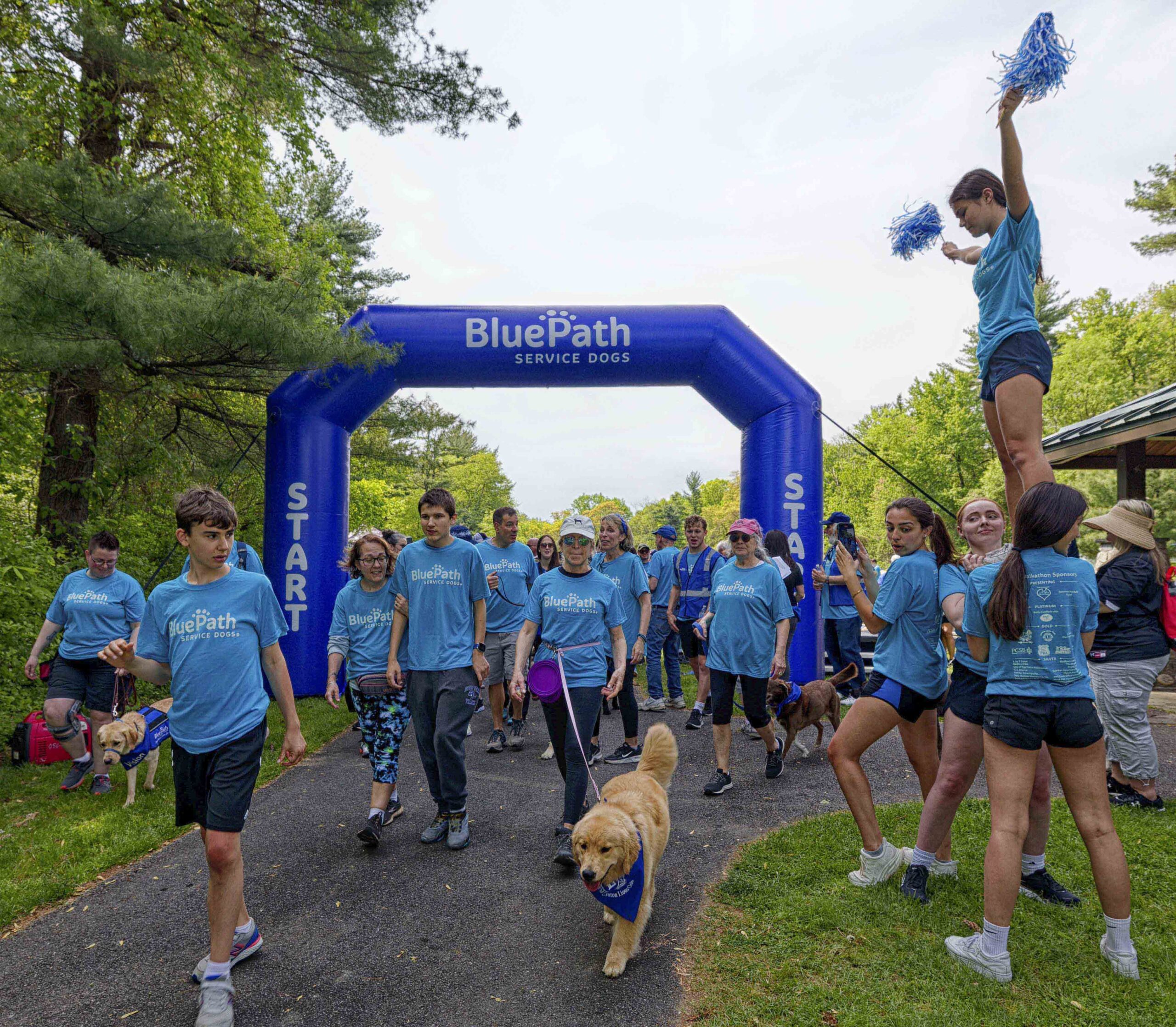 On May 13, 2023 BluePath Service Dogs held their Annual Walkathon at FDR Park in Yorktown. ThinkDIFFERENTLY was a sponsor and tabled at the event, which was attended by hundreds of people and maybe even more pups!! In this picture teams, with their dogs, start their walk with cheerleaders on their left (our right) as they began.