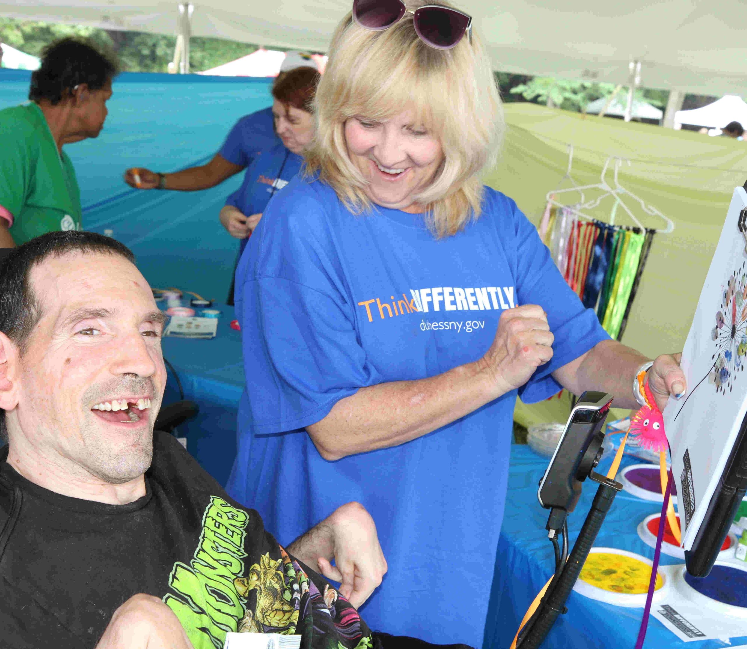 Dutchess County Early Intervention and Preschool Special Education was at hand to show families and attendees that learning is fun at all ages! Here Early Intervention staff shows a man (who is smiling wide off to the distance, and is sitting in a wheelchair) some artwork and color matching. 3rd Annual ThinkDIFFERENTLY Fitness & Field Day on Friday June 29, 2023 at Bowdoin Park.