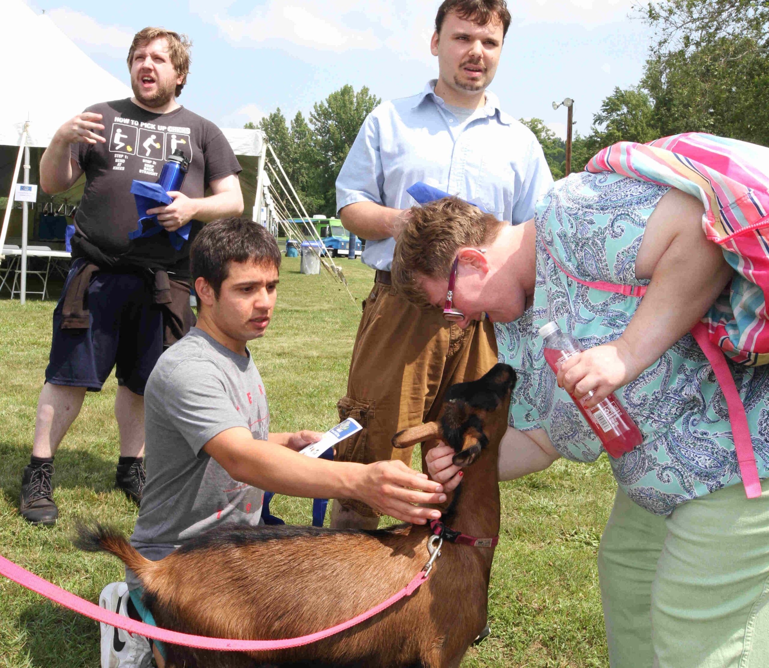 Not only did we have fun and games at the 3rd Annual ThinkDIFFERENTLY Fitness & Field Day on Friday June 29, 2023 at Bowdoin Park, we also had animals galore to pet. Here 4 individuals stand around a golden brown goat. 2 of the individuals are petting the goat, 1 of them has their face inches away from the goats face.